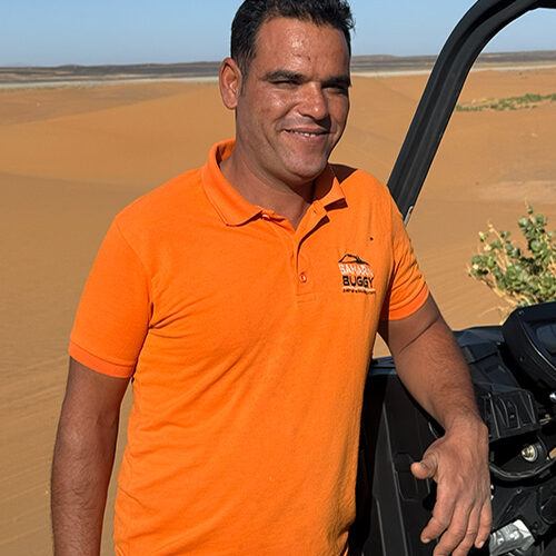 Guía del equipo de Sahara Buggy posando junto a un buggy en el desierto de Merzouga durante una jornada de rutas.