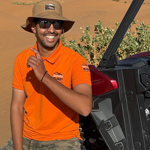 Guía de Sahara Buggy sonriendo junto a un buggy en el desierto de Merzouga durante una jornada de rutas.