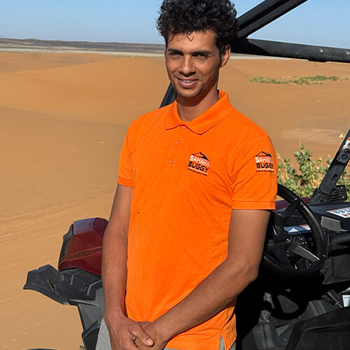 Guía de Sahara Buggy posando de pie junto a un buggy en el desierto de Merzouga durante una jornada de rutas.