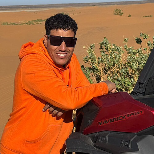 Guía de Sahara Buggy sonriendo y apoyado en un buggy en las dunas de Merzouga durante una jornada de rutas.