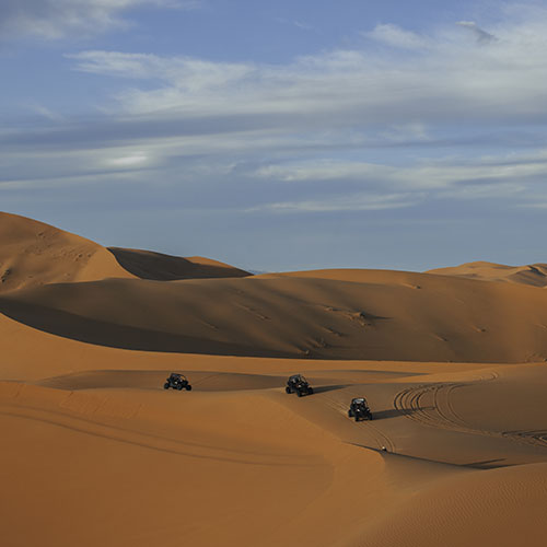 Group of Can-Am Maverick buggies driving across the golden sands of Erg Chebbi, enjoying a responsible driving experience in Merzouga