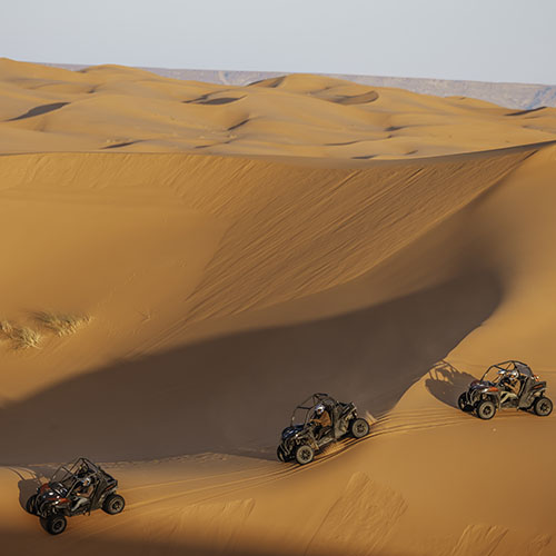 Tres buggys Can-Am Maverick de Sahara Buggy ascendiendo las dunas del Erg Chebbi durante una ruta guiada en el desierto de Merzouga, Marruecos.