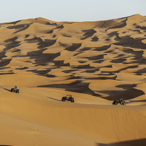 Participantes en buggy y quad recorriendo el Erg Chebbi al atardecer, con vistas panorámicas del desierto de Merzouga, Marruecos.