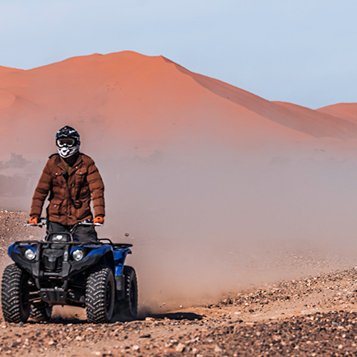 Quad and buggy tour through the Erg Chebbi desert, with dunes in the background and rocky terrain, during an adapted and safe experience with Sahara Buggy.